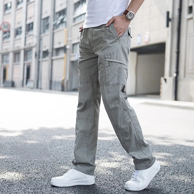 Mann in grauer Cargohose und weißen Sneakers auf städtischer Straße. Modetrend, lässiger Stil, Herrenbekleidung, Outdoor-Look.