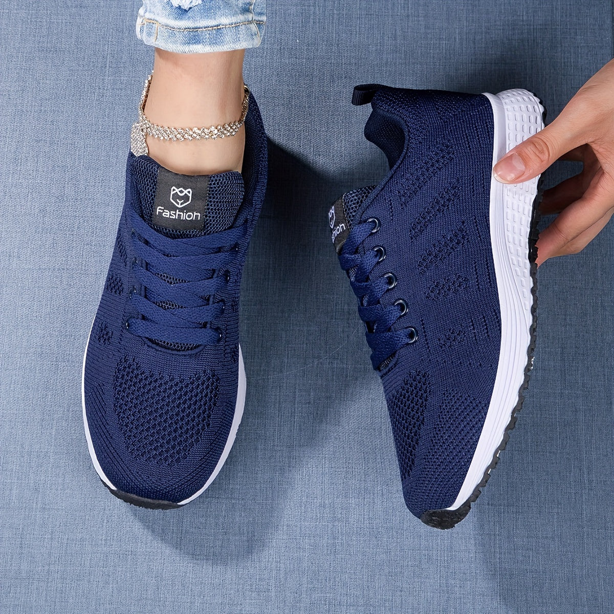 Dunkelblaue Damen-Sneaker mit weißer Sohle, modisches Design, atmungsaktives Mesh, ideal für Freizeit und Sport, auf Jeanshintergrund.