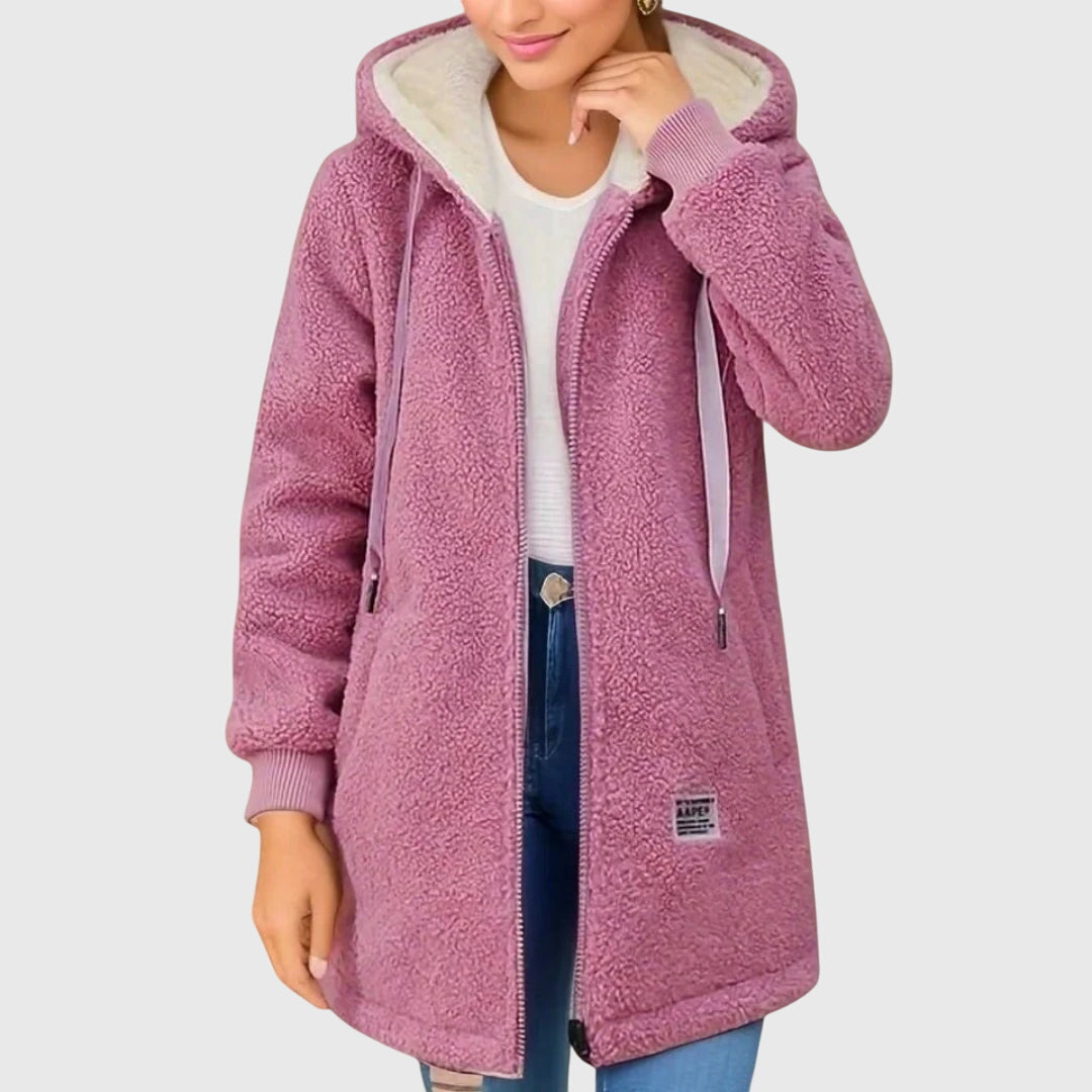 Frau trägt lila Teddyfleece-Jacke mit Kapuze, Reißverschluss und Taschen. Modische Winterbekleidung, warm und bequem. Ideal für kalte Tage.