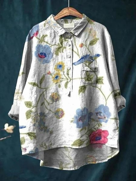 Graues Leinenhemd mit Blumenmuster und Vogelmotiv, hängend auf Holzkleiderbügel. Modisches Damenoberteil, ideal für Frühling und Sommer.