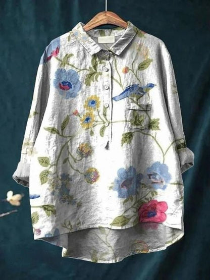 Graues Leinenhemd mit Blumenmuster und Vogelmotiv, hängend auf Holzkleiderbügel. Modisches Damenoberteil, ideal für Frühling und Sommer.
