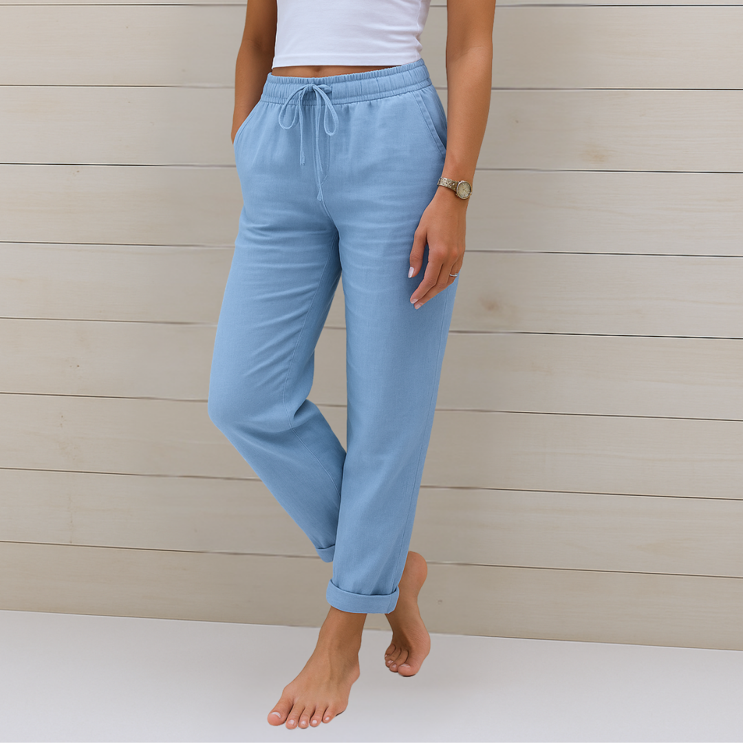 Frau in hellblauer Leinenhose und weißem Top vor Holzwand. Sommermode, bequeme Damenbekleidung, Freizeitlook, stilvolle Leinenhose.