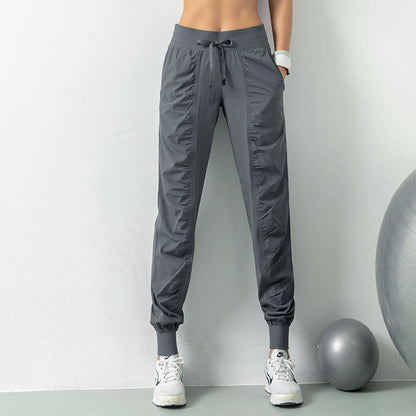 Graue Jogginghose Damen, sportlich, mit elastischem Bund und Kordelzug, kombiniert mit weißen Sneakers, Fitnessball im Hintergrund.