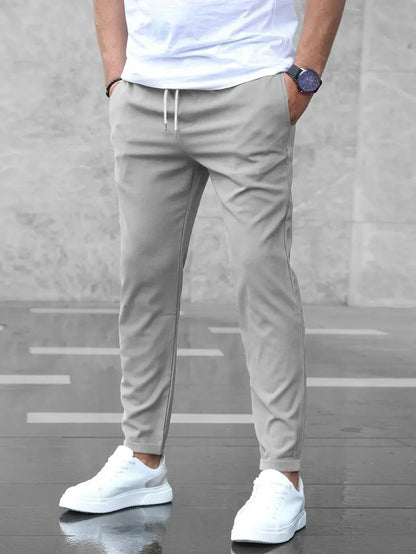 Mann in grauer Jogginghose und weißen Sneakers vor grauem Hintergrund. Lässige Herrenmode, sportlicher Look, moderne Freizeitkleidung.