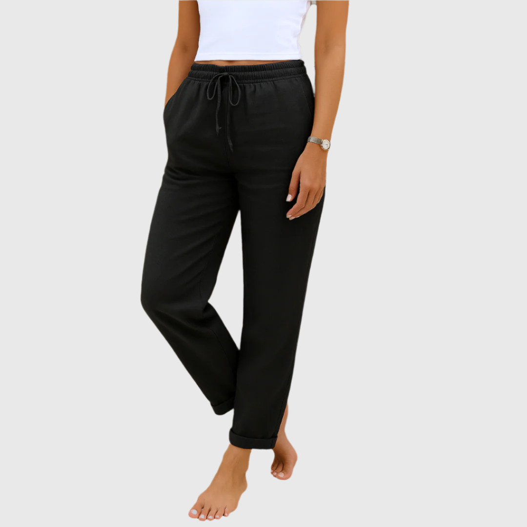 Frau in schwarzer Jogginghose und weißem Top, barfuß. Bequeme Damenmode, Freizeitlook, elastischer Bund, ideal für Zuhause oder Sport.