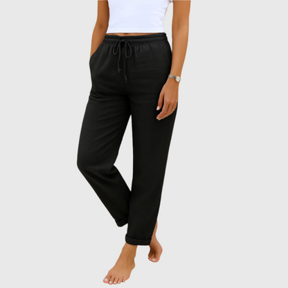 Frau in schwarzer Jogginghose und weißem Top, barfuß. Bequeme Damenmode, Freizeitlook, elastischer Bund, ideal für Zuhause oder Sport.