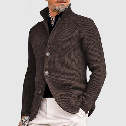 Mann in braunem Strickblazer mit Stehkragen, weißer Hose und Schal. Elegante Herrenmode, stilvoller Look, modischer Blazer für Herbst/Winter.