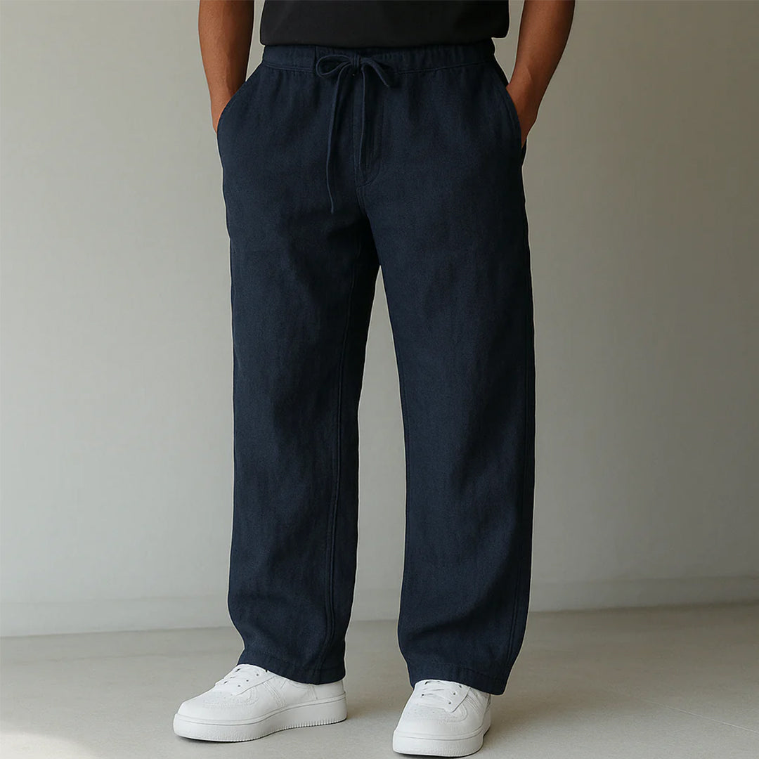 Dunkelblaue Leinenhose für Herren, locker geschnitten, mit Kordelzug und Taschen, kombiniert mit weißen Sneakern. Ideal für lässige Outfits.