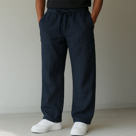 Dunkelblaue Leinenhose für Herren, locker geschnitten, mit Kordelzug und Taschen, kombiniert mit weißen Sneakern. Ideal für lässige Outfits.