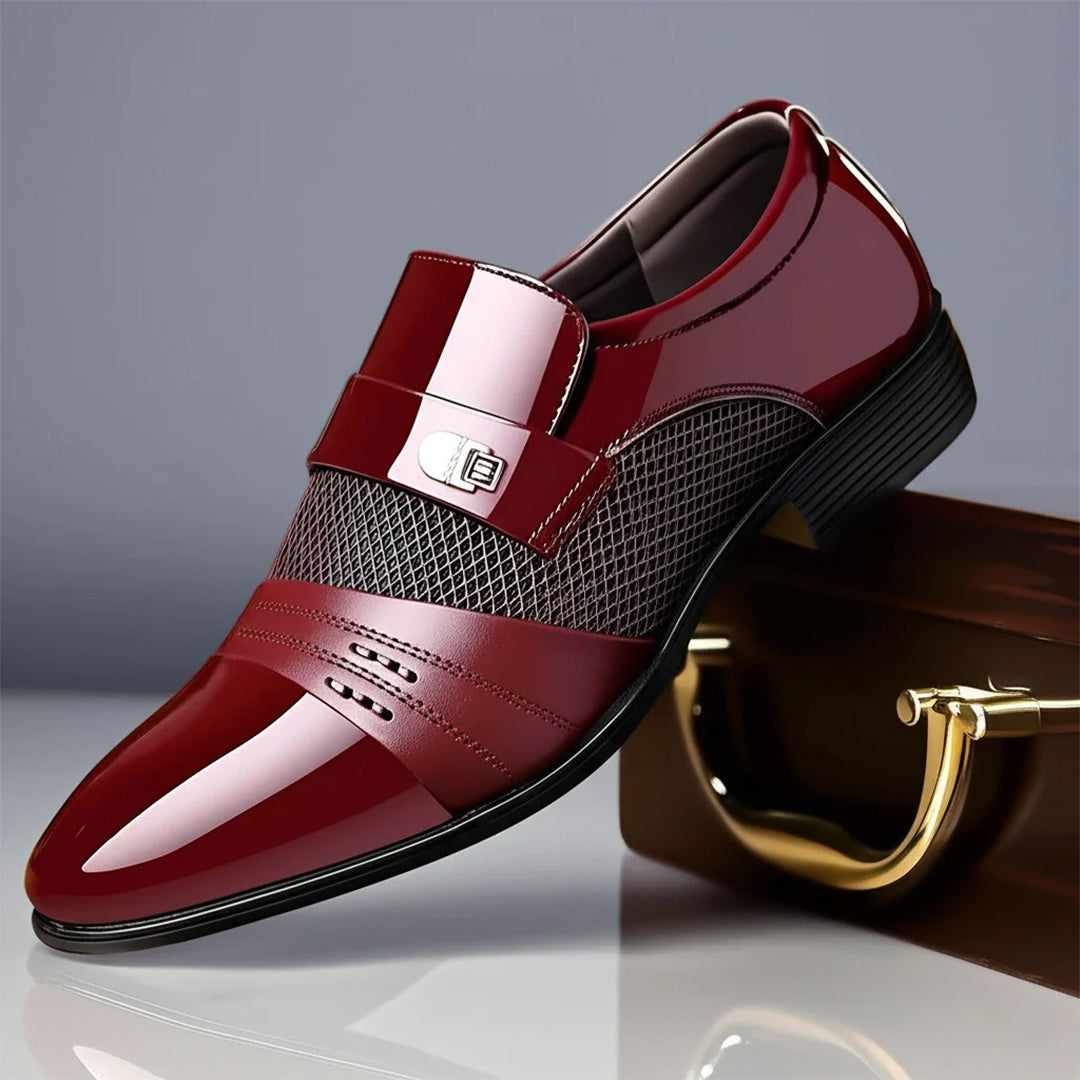 Eleganter roter Herrenschuh aus Lackleder mit Schnalle, perforiertem Design und schwarzer Sohle, auf einem braunen Koffer platziert.