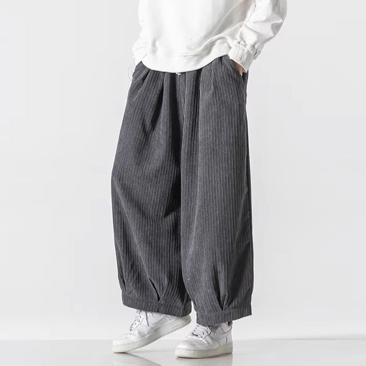 Graue, weit geschnittene Plissee-Hose aus Baumwolle, kombiniert mit weißen Sneakers und einem weißen Pullover. Modetrend, lässiger Stil.