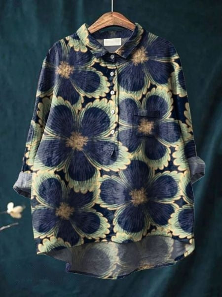 Damenbluse mit großem Blumenmuster, blau und beige, langärmlig, Knopfleiste, lässiger Stil, auf Holzkleiderbügel vor grünem Hintergrund.