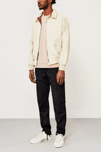 Mann in beiger Harrington-Jacke, schwarzer Hose und weißen Sneakers vor weißem Hintergrund. Modischer Freizeitlook für Herren.