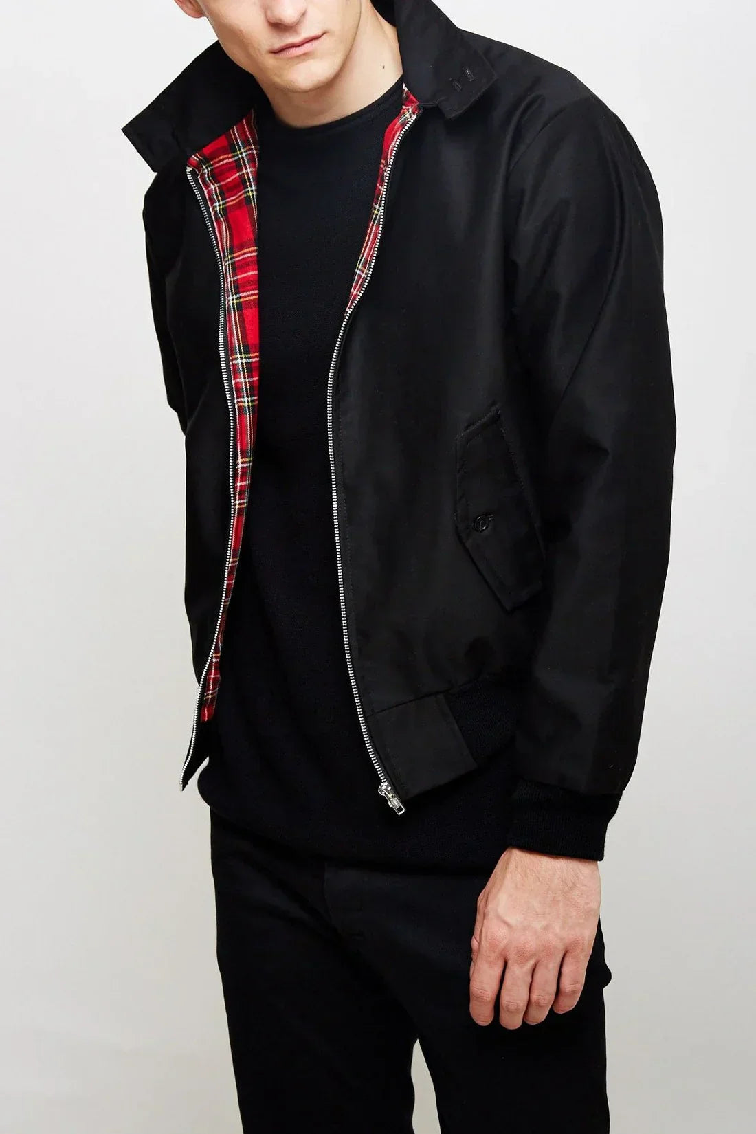 Mann trägt schwarze Harrington-Jacke mit rotem Karofutter, Reißverschluss und Taschen. Modische Herrenbekleidung, klassischer Stil, Herbstmode.