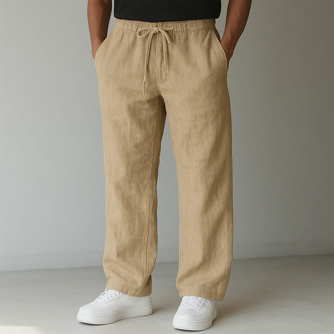 Beige Leinenhose für Herren, lässig geschnitten, mit Kordelzug, kombiniert mit weißen Sneakern. Ideal für Sommermode und Freizeitkleidung.