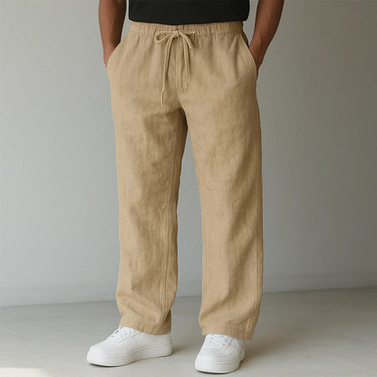 Beige Leinenhose für Herren, lässig geschnitten, mit Kordelzug, kombiniert mit weißen Sneakern. Ideal für Sommermode und Freizeitkleidung.