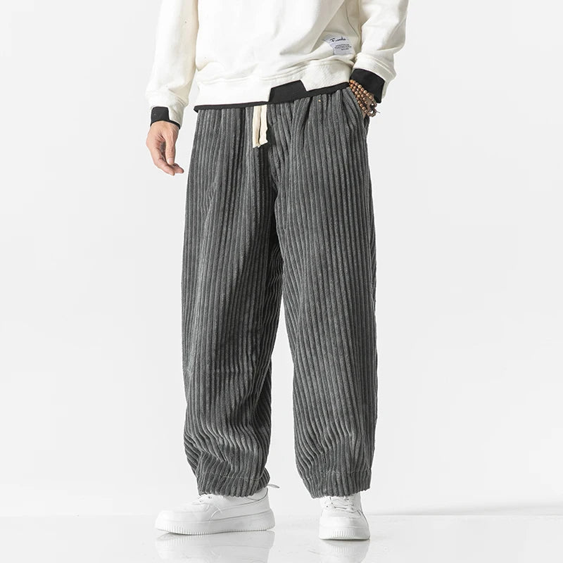 Graue Cordhose für Herren, lässig geschnitten, kombiniert mit weißem Sweatshirt und Sneakers. Modetrend, bequeme Herrenbekleidung, Freizeitlook.