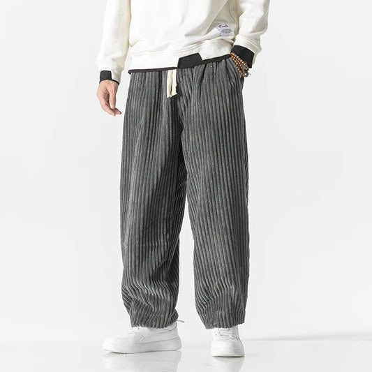 Graue Cordhose für Herren, lässig geschnitten, kombiniert mit weißem Sweatshirt und Sneakers. Modetrend, bequeme Herrenbekleidung, Freizeitlook.
