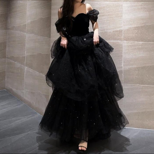 Frau in elegantem, schwarzem Abendkleid mit Tüll und Pailletten, steht in modernem, minimalistischem Raum. Abendmode, Ballkleid, Glamour.