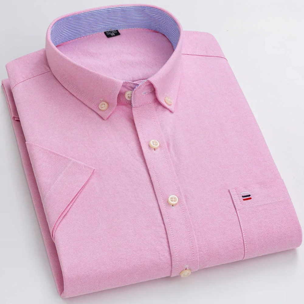 Gefaltetes rosa Herrenhemd mit Button-Down-Kragen, Brusttasche und gesticktem Logo. Elegantes Design, ideal für Business- und Freizeitkleidung.