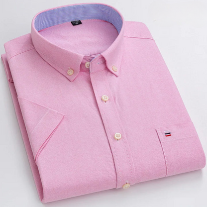 Gefaltetes rosa Herrenhemd mit Button-Down-Kragen, Brusttasche und gesticktem Logo. Elegantes Design, ideal für Business- und Freizeitkleidung.