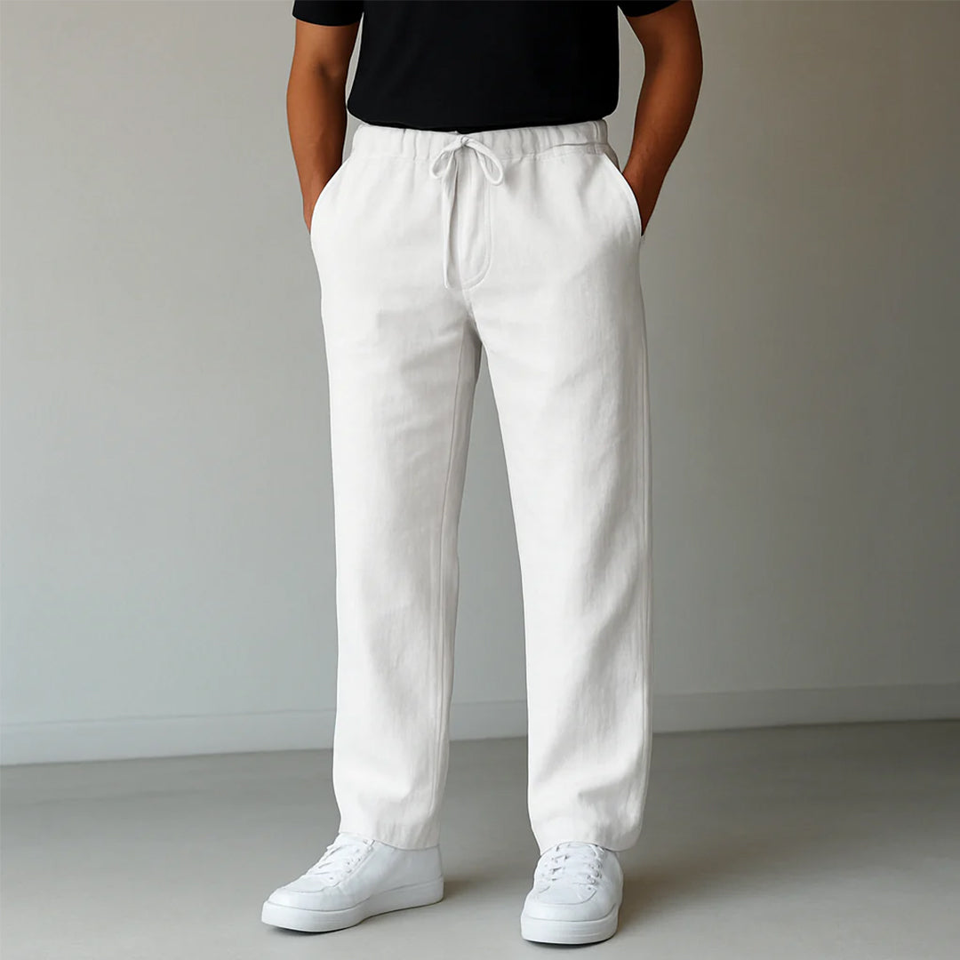 Weiße Leinenhose für Herren, lässig geschnitten, mit Kordelzug, kombiniert mit weißen Sneakern und schwarzem T-Shirt. Ideal für Sommermode.