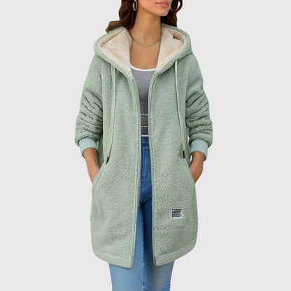 Frau in mintgrünem Teddy-Fleece-Mantel mit Kapuze, lässig über grauem Top und blauer Jeans getragen. Modetrend, Damenmode, Herbst/Winter-Outfit.