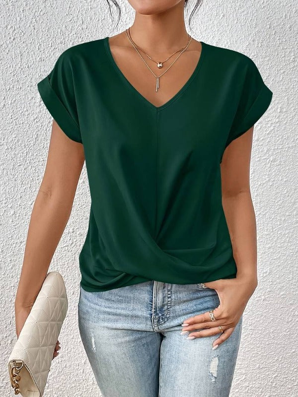 Frau in dunkelgrünem V-Ausschnitt-Shirt, hellblauer Jeans, hält weiße gesteppte Clutch. Modetrend, lässiger Look, Damenmode.