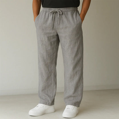 Graue Leinenhose für Herren, locker geschnitten mit Kordelzug, kombiniert mit weißen Sneakern. Ideal für lässige Sommermode und Komfort.