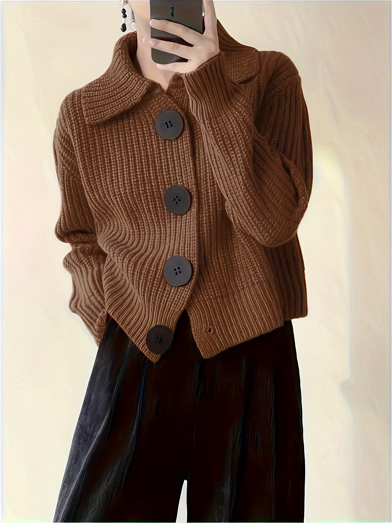 Braune Strickjacke mit großen Knöpfen, getragen von Person, die ein Smartphone hält. Modetrend, Herbstmode, Damenbekleidung, stilvoller Look.