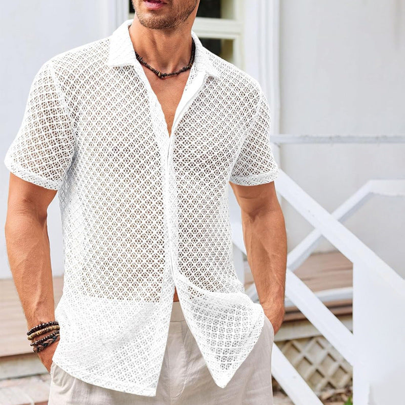 Mann in weißem, durchsichtigen Häkelhemd, lässig und stilvoll, steht vor einem modernen Gebäude. Sommermode, Herrenbekleidung, Freizeitlook.