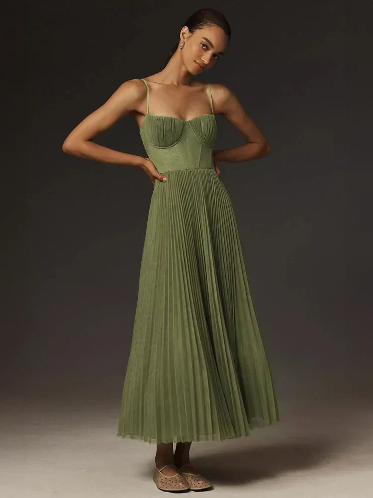 Frau in langem, grünem, plissiertem Kleid mit Spaghettiträgern, posiert vor dunklem Hintergrund. Elegantes Abendkleid, Mode, Damenbekleidung.
