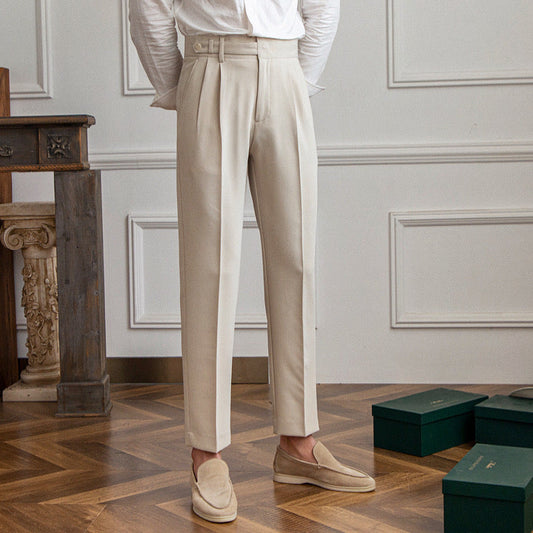Elegante beige Anzughose für Herren, kombiniert mit beigen Loafers, auf Parkettboden vor weißer Wand. Perfekt für formelle Anlässe und Business-Outfits.
