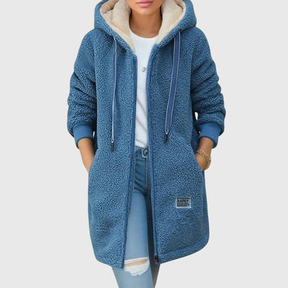 Frau in blauem Teddyfell-Mantel mit Kapuze, weißem Shirt und zerrissener Jeans. Modischer Winterlook, gemütlich und stilvoll.