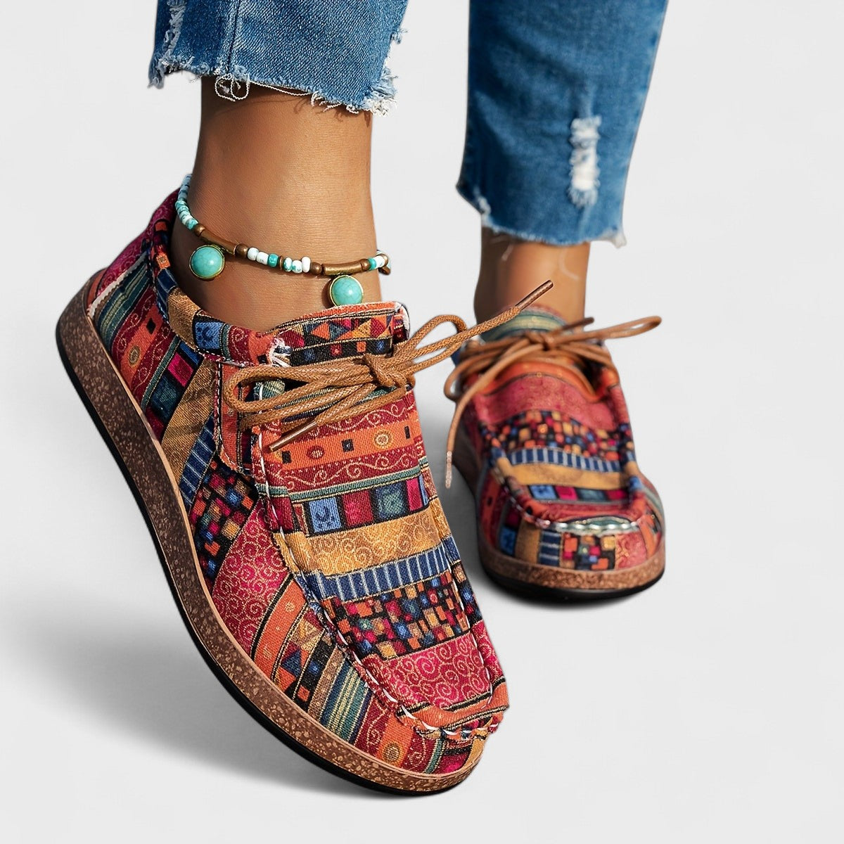 Bunte Damen-Sneaker mit Ethno-Muster, kombiniert mit blauen Jeans und türkisfarbenem Fußkettchen. Modische Freizeitschuhe für Frauen.