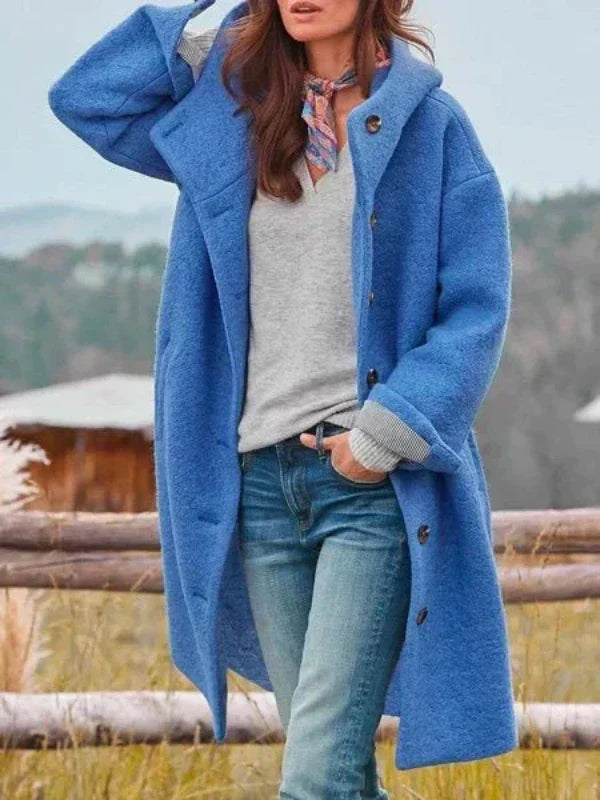 Frau in blauem Wollmantel, grauem Pullover und Jeans vor ländlicher Kulisse. Herbstmode, stilvoller Look, Outdoor-Bekleidung.
