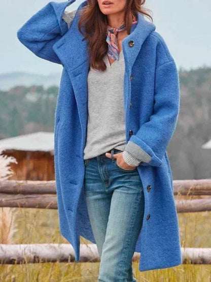 Frau in blauem Wollmantel, grauem Pullover und Jeans vor ländlicher Kulisse. Herbstmode, stilvoller Look, Outdoor-Bekleidung.