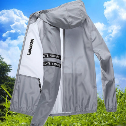 Graue Windjacke mit Kapuze, Schriftzug "LOCAPPOLE" auf dem Ärmel, vor blauem Himmel und grüner Wiese. Leichte Outdoor-Jacke für Herren.
