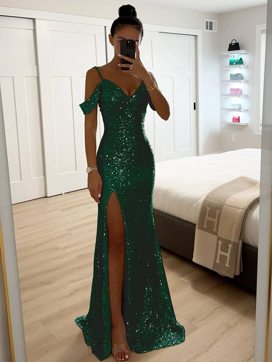 Frau im eleganten, grünen Paillettenkleid mit Schlitz, steht in modernem Schlafzimmer, macht Selfie. Abendmode, glamouröses Outfit, Modefotografie.