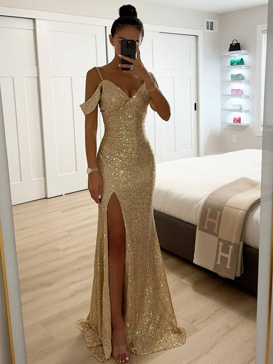 Frau in funkelndem, goldenen Abendkleid mit hohem Beinschlitz, steht in modernem Schlafzimmer, macht Selfie im Spiegel. Elegantes Abendmode-Outfit.