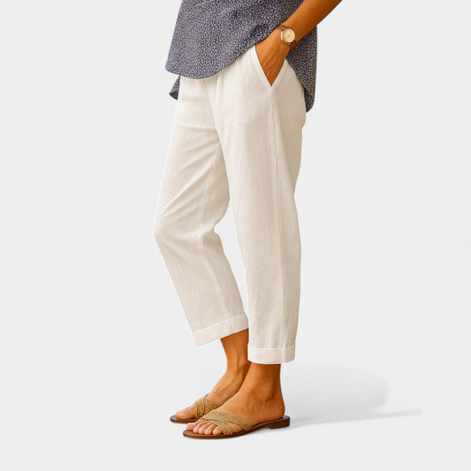 Damenhose aus weißem Leinen, kombiniert mit braunen Sandalen und einer gemusterten Bluse. Sommermode, lässiger Stil, bequeme Kleidung.