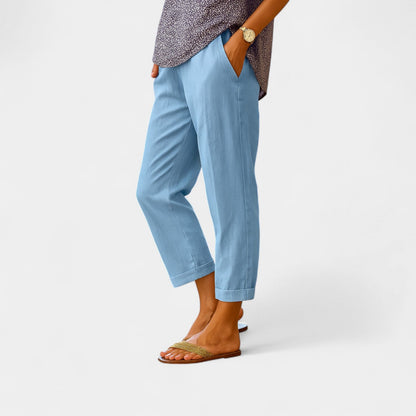 Frau trägt hellblaue Leinenhose, kombiniert mit Sandalen und gemustertem Oberteil. Sommermode, bequeme Damenbekleidung, Freizeitlook.