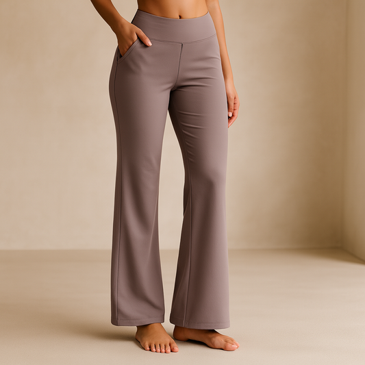 Frau in brauner, ausgestellter Yogahose, barfuß, in neutralem Raum. Bequeme, modische Sportbekleidung für Yoga und Fitness.