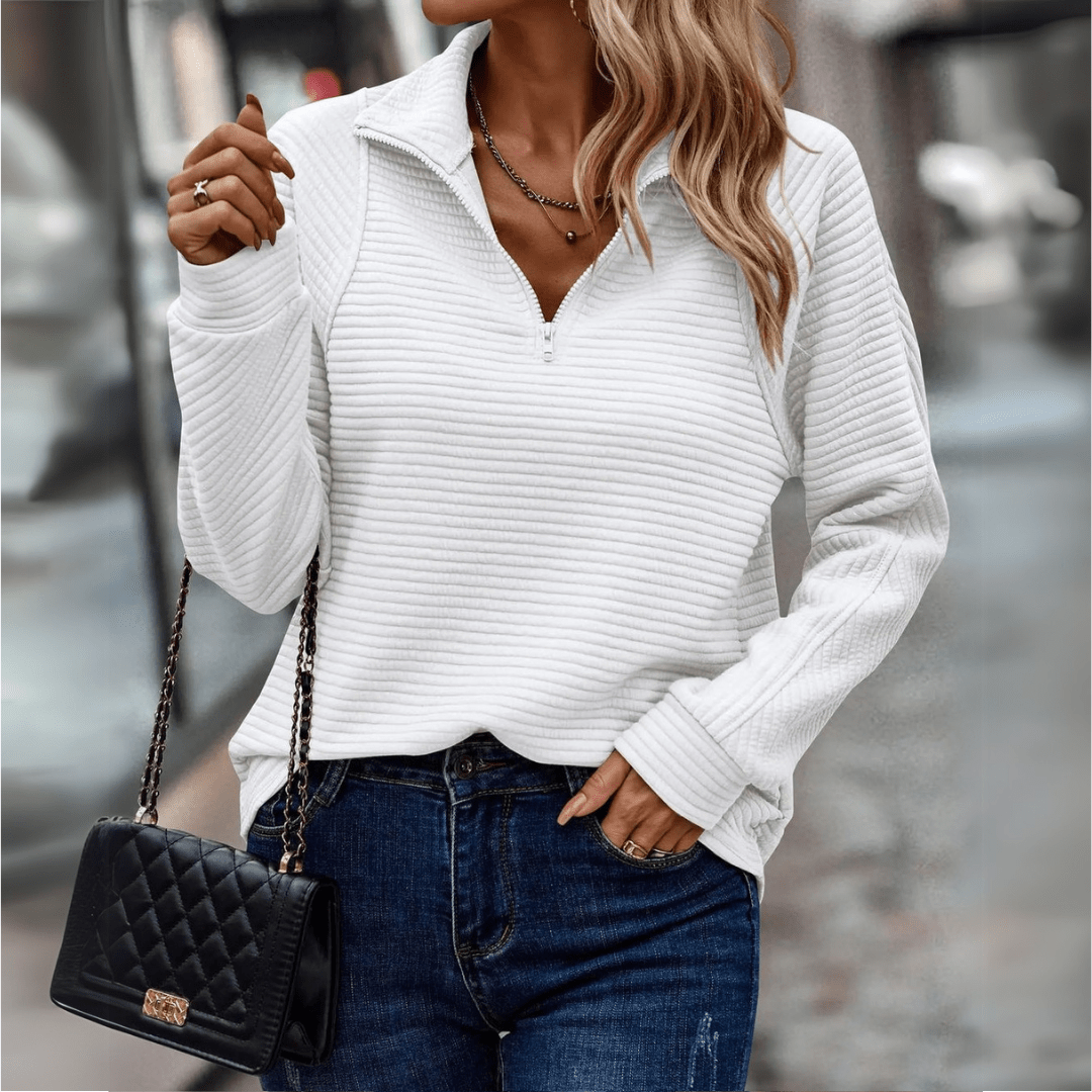 Frau in weißem Pullover mit Reißverschluss, blauer Jeans und schwarzer gesteppter Handtasche. Modetrend, Herbstmode, Streetstyle.