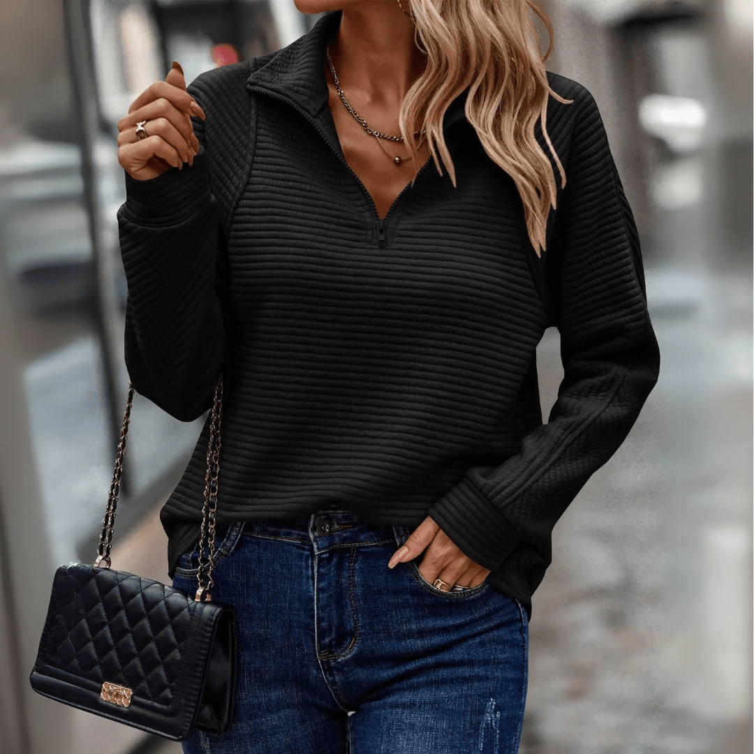 Frau in schwarzem, geripptem Pullover und blauen Jeans, hält eine gesteppte Handtasche. Modetrend, Herbstmode, Streetstyle.