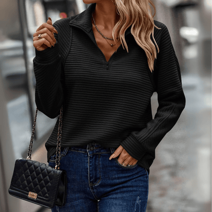 Frau in schwarzem, geripptem Pullover und blauen Jeans, hält eine gesteppte Handtasche. Modetrend, Herbstmode, Streetstyle.