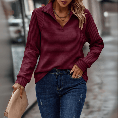 Frau in bordeauxrotem Pullover und blauer Jeans, hält eine beige Clutch. Modetrend Herbst, lässiger Streetstyle, stilvolle Damenbekleidung.