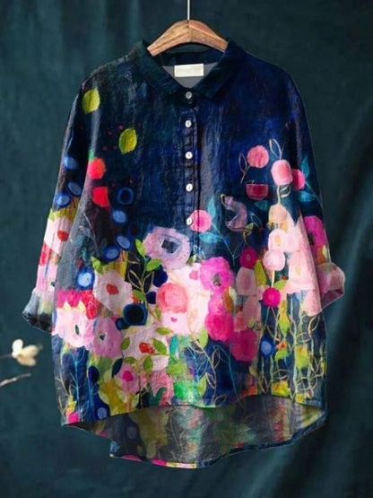 Bunte Damenbluse mit floralem Muster, Aquarell-Design, Knopfleiste, hängend auf Holzkleiderbügel vor dunklem Hintergrund.