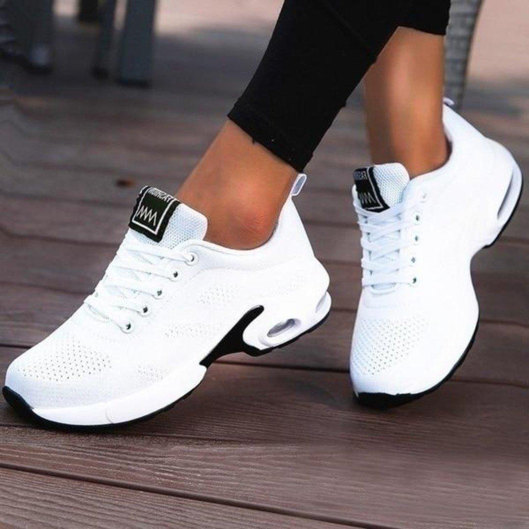 Weiße Damen-Sneaker mit Luftpolstersohle auf Holzterrasse. Modische Sportschuhe, bequem und atmungsaktiv, ideal für Freizeit und Sport.
