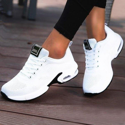 Weiße Damen-Sneaker mit Luftpolstersohle auf Holzterrasse. Modische Sportschuhe, bequem und atmungsaktiv, ideal für Freizeit und Sport.